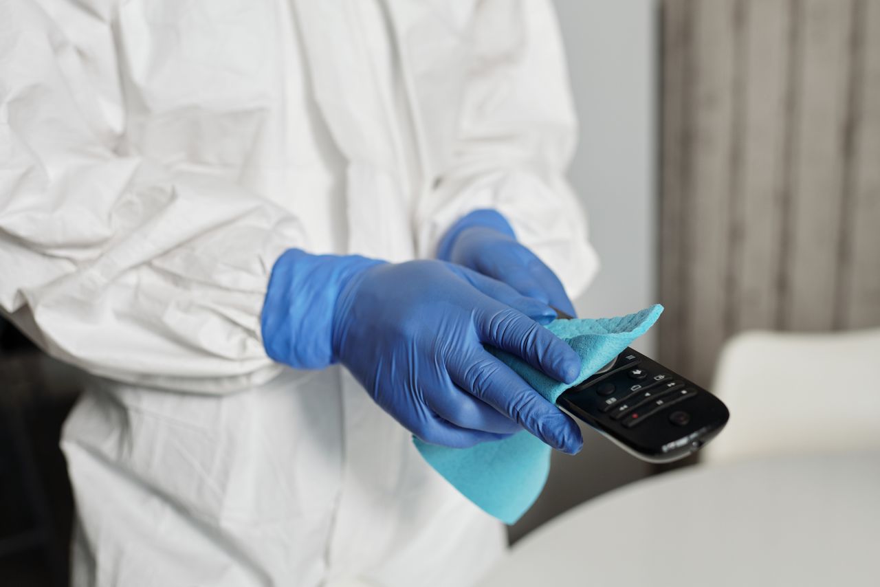 services-02 Close-up of a person disinfecting a remote control wearing protective gloves, ensuring cleanliness.